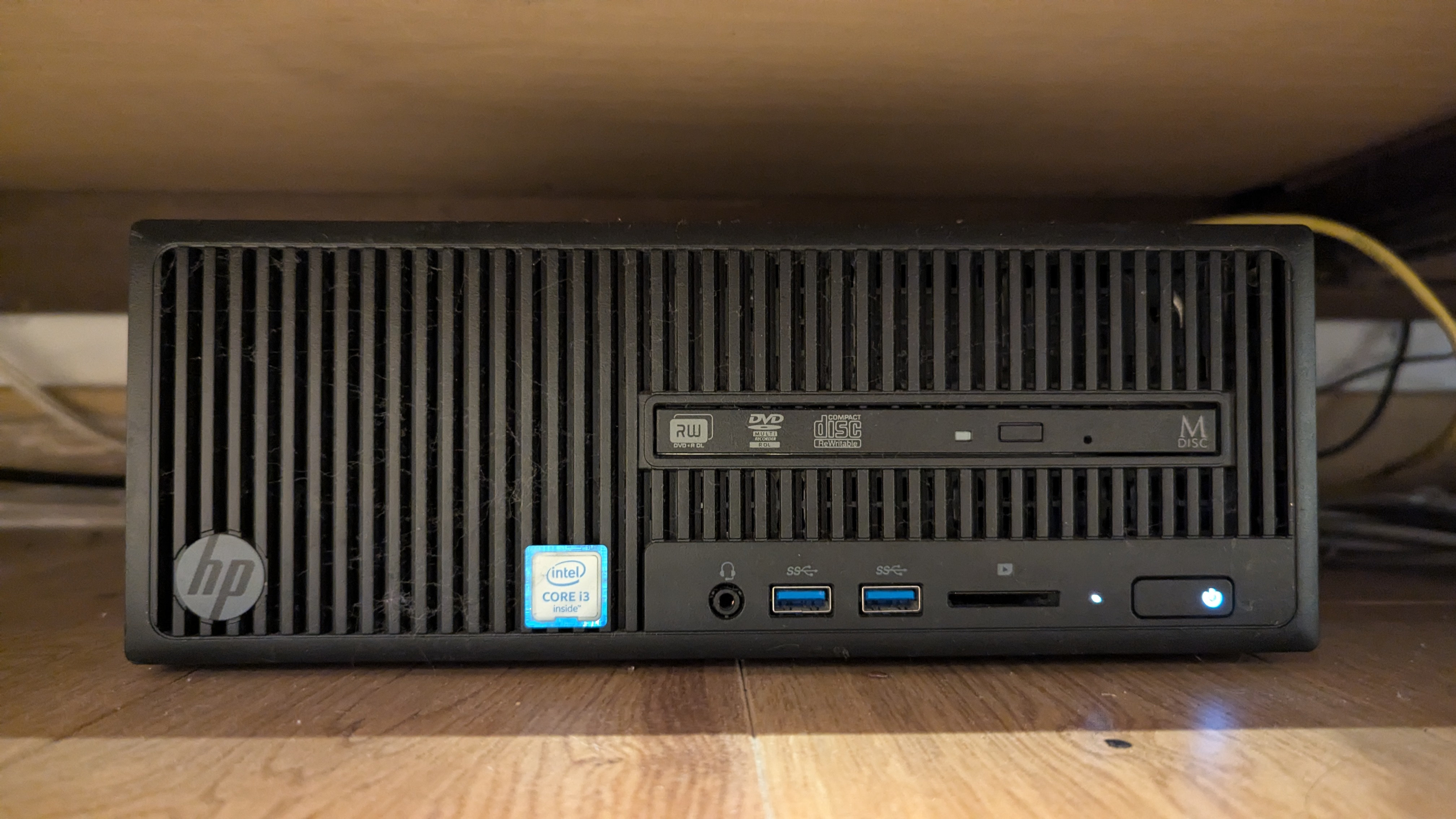 A slightly dusty HP 280 G2 SFF computer, under a chest of drawers with a yellow ethernet cable running off somwhere from behind.