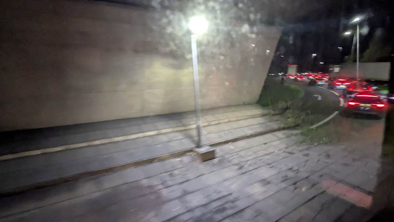 A blurry photo of a lamp post under an overpass with a traffic jam visible on the right of the image, the only light sources are the lamp post and the brake lights of the cars.